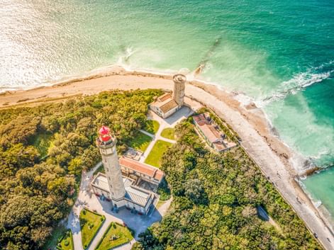 Luftaufnahme des Leuchtturmkomplexes Phare des Baleines auf der Île de Ré mit zwei Leuchttürmen und Gebäuden an einer Küstenspitze mit türkisfarbenem Wasser.
