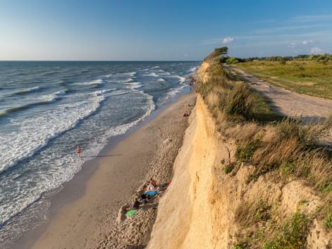 Sandige Steilküste mit Gras oben mit Blick auf die Ostsee bei Prerow. Radfahrer ruhen am Strand unten, während Wellen ans Ufer rollen.