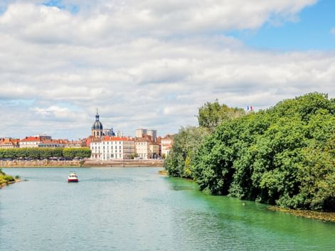 Blick auf die Saône in Chalon-sur-Saône mit grünen Bäumen am Ufer, einem kleinen Boot auf dem Wasser und historischen Gebäuden unter blauem Himmel.