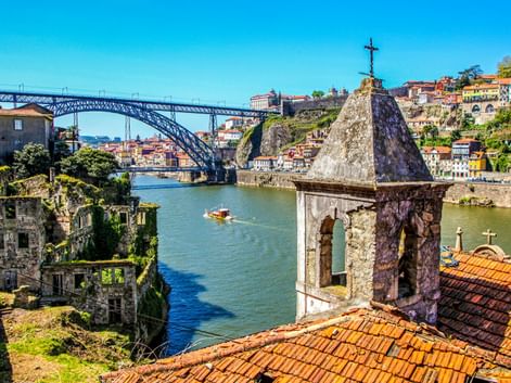 Blick auf die Ponte Dom Luís I in Porto über dem Douro, mit Kirchturm im Vordergrund und bunten Häusern am Hang.