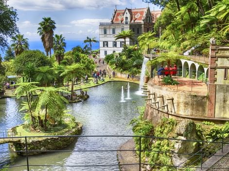 Terrassierter tropischer Garten in Funchal, Madeira mit Teichen, Springbrunnen, üppiger Vegetation und weißem Palast mit rotem Dach.