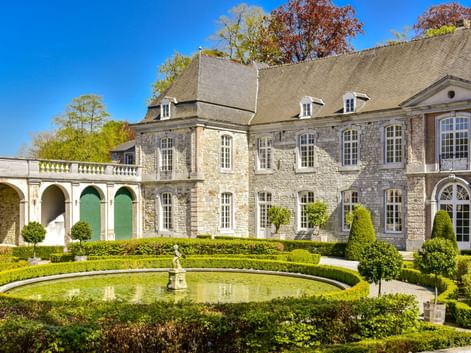 Steinschloss mit formalen Wassergärten in Annevoie mit rundem Springbrunnenbecken, umgeben von gepflegten Hecken und Formgehölzen.