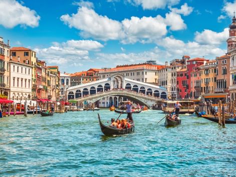 Rialtobrücke über dem Canale Grande in Venedig mit Gondeln und Booten im türkisfarbenen Wasser. Bunte historische Gebäude säumen beide Seiten.