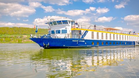Flusskreuzfahrtschiff MS Prinzessin Katharina mit blauem Rumpf und weißem Aufbau fährt auf der Donau unter teilweise bewölktem Himmel.
