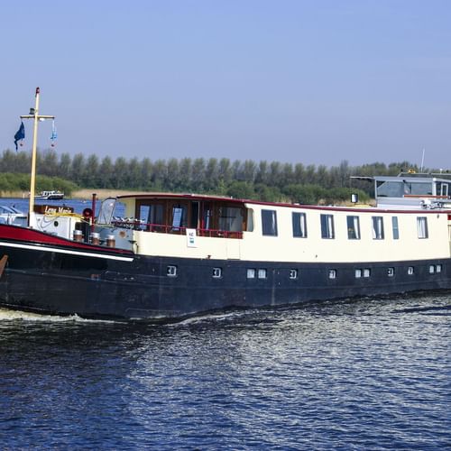 MS Lena Maria, ein Passagierschiff mit dunkelblauem Rumpf und weißem Aufbau, fährt auf einem Fluss mit Bäumen am Ufer.