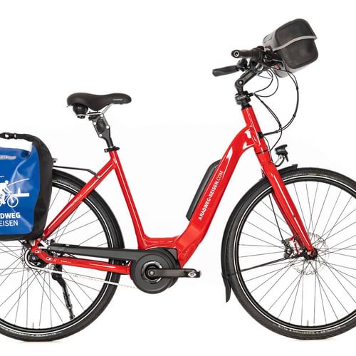 Rotes Tiefeinsteiger-E-Bike mit schwarzem Sattel, Lenkertasche und blauer Radweg Reisen Packtasche am Gepäckträger, vor weißem Hintergrund.