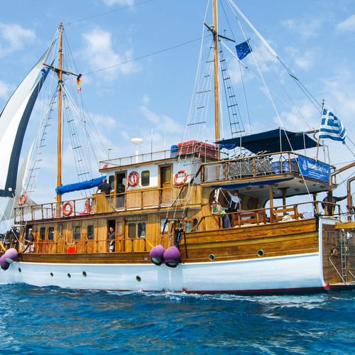 MS Panagiota, ein hölzernes Segelschiff mit weißem Rumpf und zwei Masten, segelt auf blauem Meer unter klarem Himmel mit griechischer Flagge.