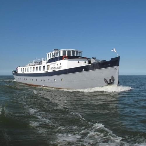 Weiß-dunkelblaues Passagierschiff Floor van Aemstel fährt auf offenem Wasser unter klarem blauen Himmel und erzeugt eine Bugwelle.