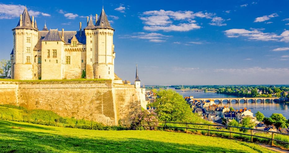 Château de Saumur, ein weißes mittelalterliches Schloss mit Türmen, auf einem Hügel mit Blick auf die Loire und die Stadt Saumur mit Brücke.