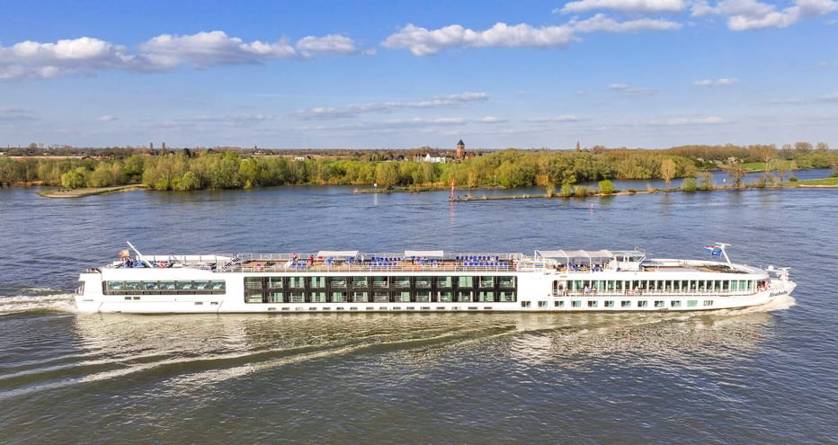 Weißes Flusskreuzfahrtschiff MS Lisabelle auf der Donau mit grünem bewaldeten Ufer und blauem Himmel im Hintergrund.