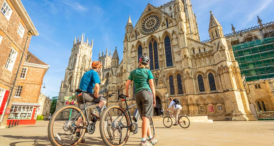 Zwei Radfahrer mit Rädern vor der Kathedrale York Minster in Yorkshire. Die gotische Kathedrale zeigt eine große Rosette und ornamentale Fassade.