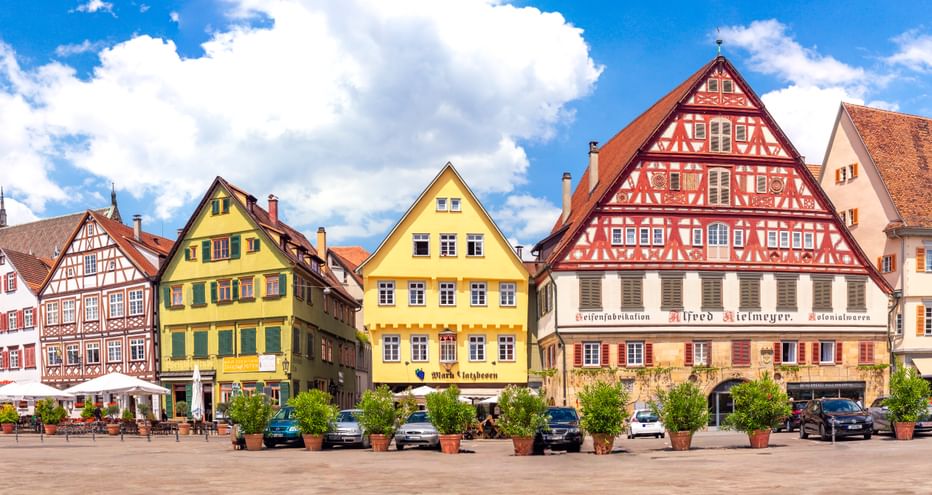 Panoramablick auf den Esslinger Marktplatz mit bunten Fachwerkhäusern, Kirchturm und parkenden Autos unter blauem Himmel mit Wolken.