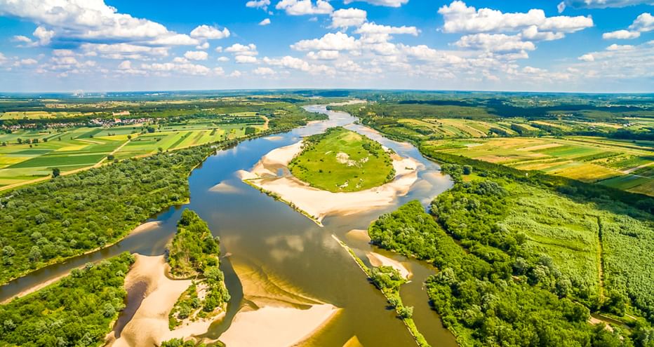 Luftaufnahme der Weichsel, die sich durch grüne Felder und Wälder in Polen schlängelt, unter blauem Himmel mit weißen Wolken.