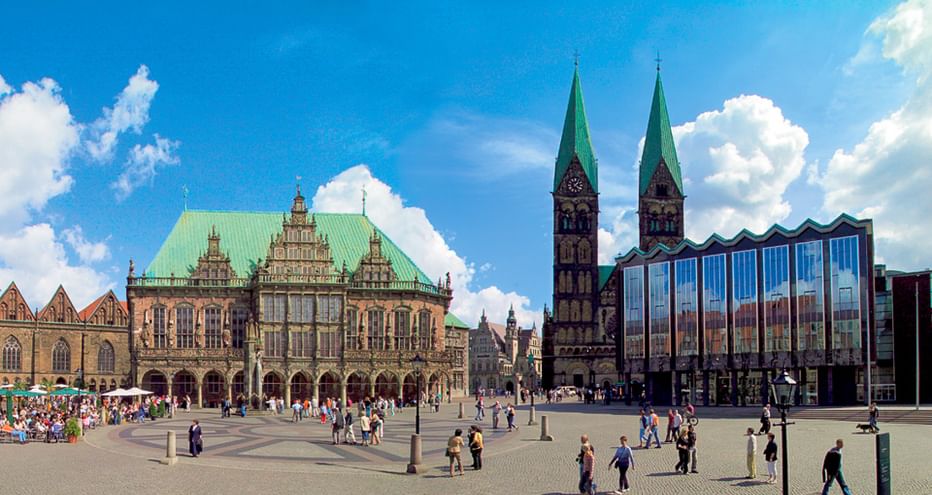 Bremen Market Square with historic Town Hall featuring green copper roof, twin-spired cathedral, and modern glass building under blue sky.