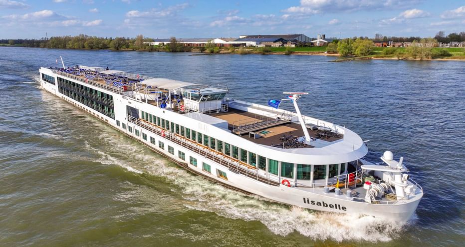 Weißes Flusskreuzfahrtschiff Lisabelle fährt auf der Donau mit grünen Ufern und blauem Himmel im Hintergrund.