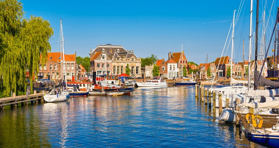 Yachthafen in Enkhuizen mit Segelbooten am Ufer. Historische niederländische Gebäude mit orangen Dächern säumen den Hafen unter blauem Himmel.