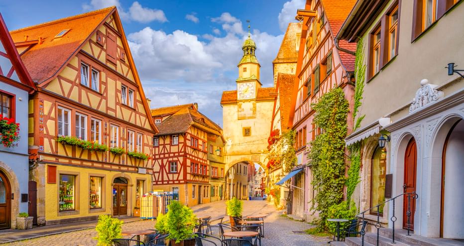 Historische Straße in Rothenburg ob der Tauber mit bunten Fachwerkhäusern, Markusturm mit grüner Spitze und Röderbogen.