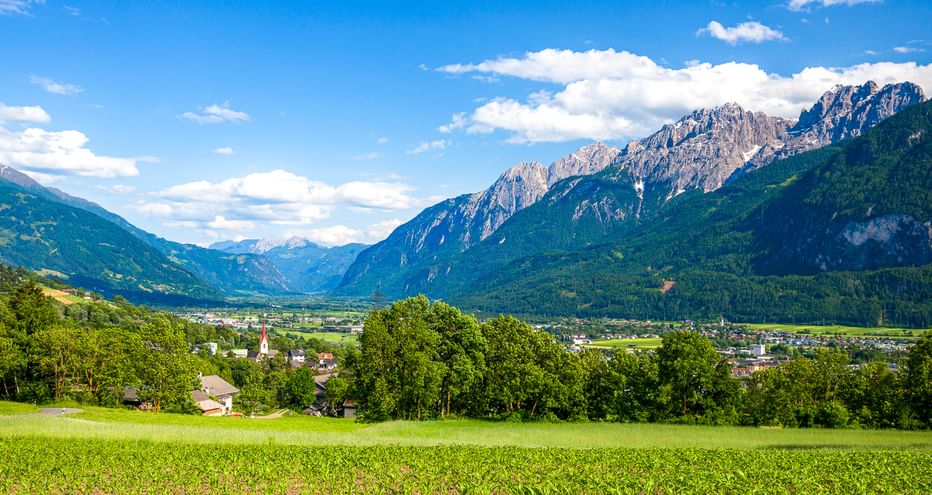 Grüne Wiese im Vordergrund mit Blick auf Lienz und das Tal, umgeben von den markanten Gipfeln der Lienzer Dolomiten unter blauem Himmel.
