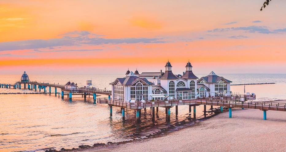 Historische Seebrücke Sellin mit weißem Pavillon auf Holzpfählen, die bei Sonnenuntergang in die Ostsee ragt.