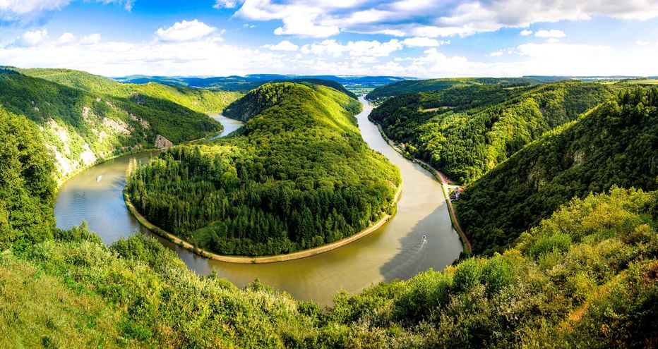 Luftaufnahme der Saarschleife, einer dramatischen Flussschleife der Saar, umgeben von dicht bewaldeten Hügeln unter blauem Himmel.
