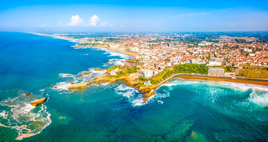 Luftaufnahme von Biarritz, Frankreich mit Atlantikküste, felsigen Klippen, Stränden und der Stadt unter blauem Himmel.