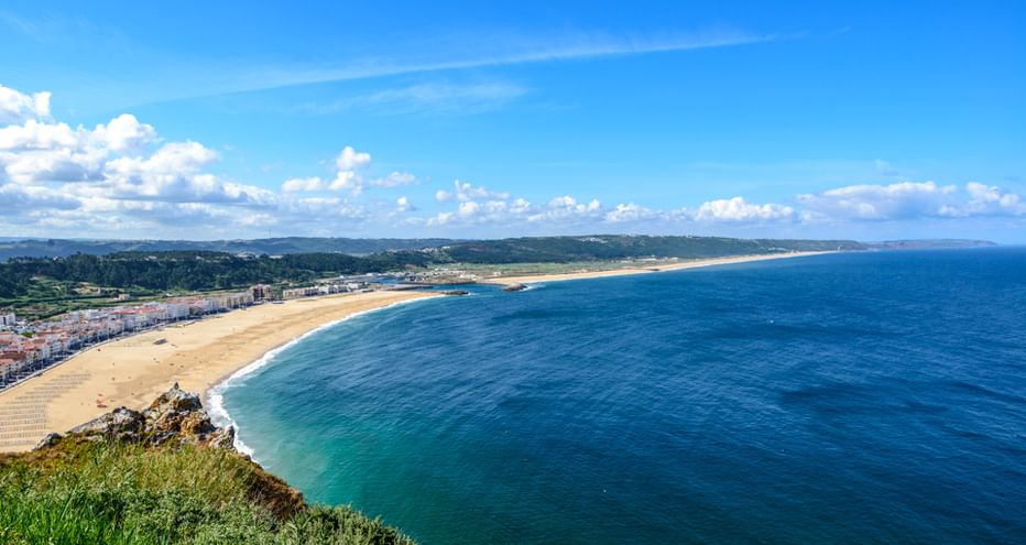 Panoramablick auf einen langen Sandstrand und blaues Meer entlang der portugiesischen Küste zwischen Porto und Lissabon unter hellem Himmel.