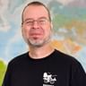Portrait von Michael K. mit Brille und schwarzem Radfahrer-Shirt mit Weltkarte im Hintergrund.
