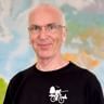 Portrait von Dieter mit Brille und schwarzem Radfahrer-Shirt mit weißer Radfahrer-Grafik, stehend vor einer bunten Weltkarte.