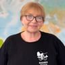 Suzanne mit Brille und schwarzem Radweg-Reisen T-Shirt mit Radfahrer-Logo, stehend vor einer Weltkarte im Hintergrund.